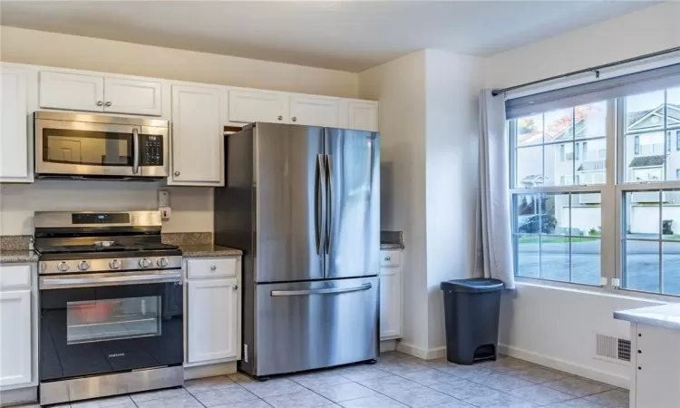 Kitchen with white cabinets, dark stone countertops, stainless steel appliances, and light tile patterned floors