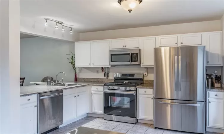 Kitchen with white cabinets, stainless steel appliances, sink, and stone countertops