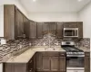 Modern kitchen featuring light stone countertops, dark brown cabinets, appliances with stainless steel finishes, backsplash and sink