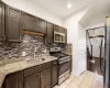 Kitchen with dark brown cabinets, stainless steel appliances, backsplash, sink, and light stone counters