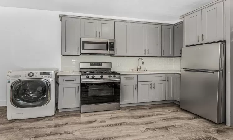 Kitchen featuring gray cabinets, stainless steel appliances, washer / dryer, and light hardwood / wood-style flooring