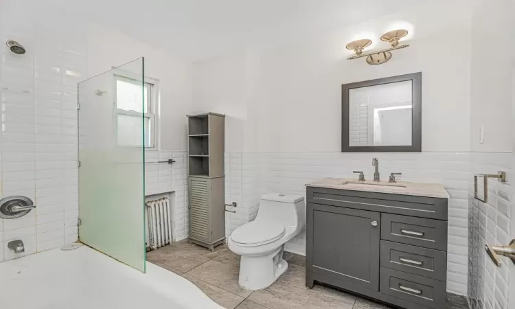 Bathroom featuring toilet, vanity, tile patterned flooring, and tile walls