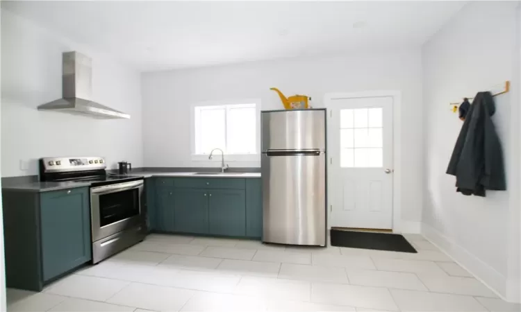 Kitchen with appliances with stainless steel finishes, light tile patterned flooring, sink, and wall chimney range hood