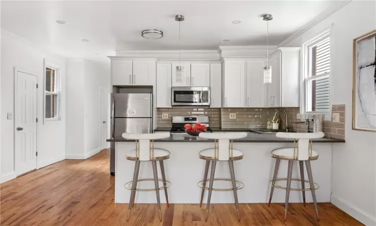 Kitchen with appliances with stainless steel finishes, a kitchen breakfast bar, white cabinetry, decorative light fixtures, and light hardwood / wood-style flooring