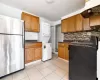 Kitchen featuring stacked washer and clothes dryer, backsplash, ventilation hood, light tile patterned flooring, and stainless steel refrigerator