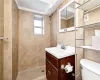 Bathroom featuring toilet, tile patterned floors, tile walls, tiled shower, and vanity