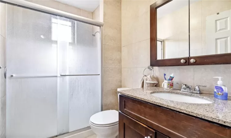 Bathroom with tasteful backsplash, a shower with door, tile walls, toilet, and vanity