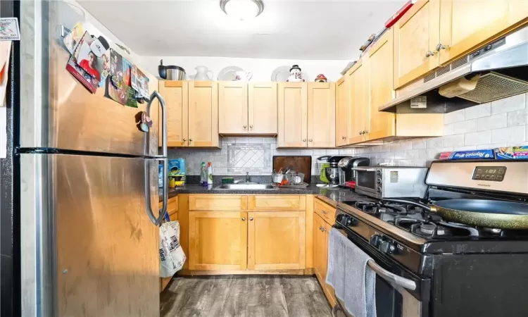 Kitchen with sink, backsplash, stainless steel appliances, light brown cabinets, and dark hardwood / wood-style floors