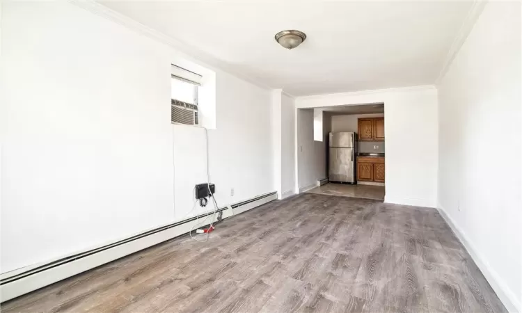 Empty room featuring cooling unit, crown molding, baseboard heating, and light wood-type flooring