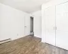 Unfurnished bedroom with a closet, dark hardwood / wood-style flooring, and a baseboard heating unit