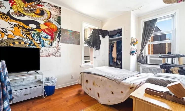 Bedroom with hardwood / wood-style floors, crown molding, and a closet