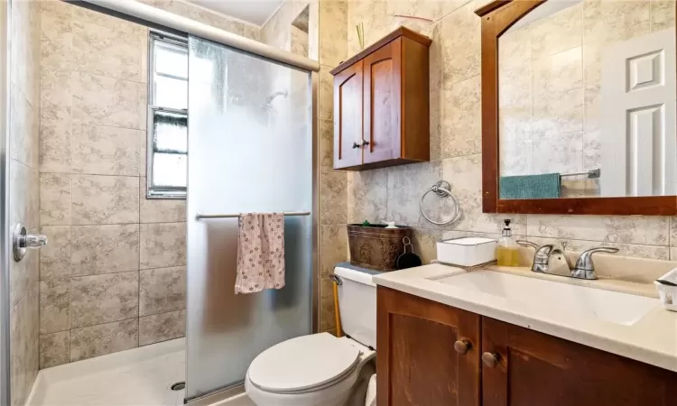 Bathroom featuring tile walls, vanity, toilet, and walk in shower