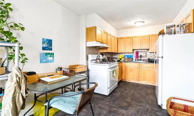 Kitchen with white appliances, light brown cabinetry, sink, backsplash, and a textured ceiling