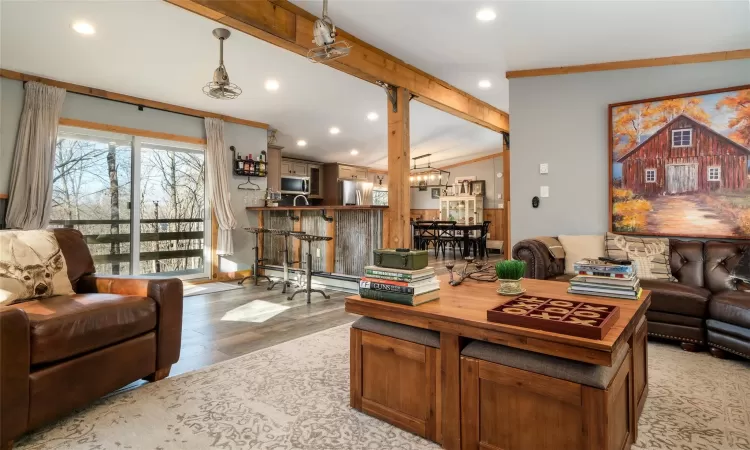 Living room featuring baseboard heating, crown molding, light hardwood / wood-style flooring, a notable chandelier, and vaulted ceiling with beams