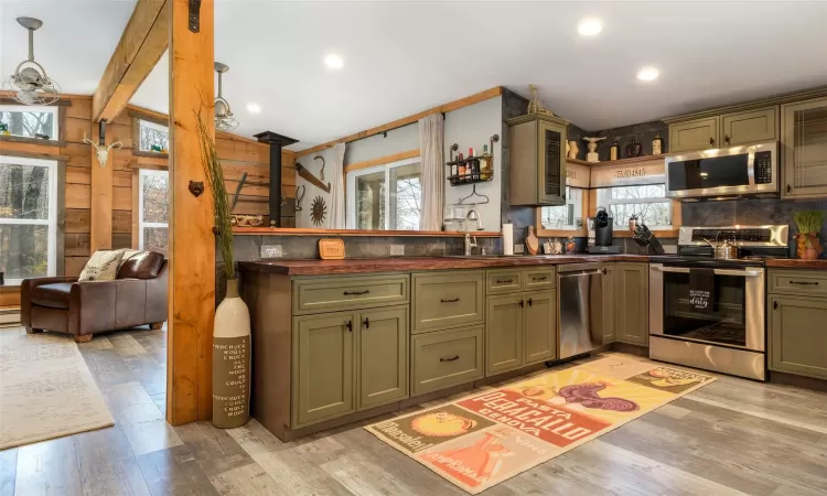 Kitchen featuring appliances with stainless steel finishes, light wood-type flooring, decorative light fixtures, and a wood stove