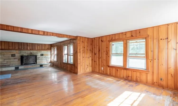 Unfurnished living room featuring wooden walls, light wood-type flooring, and a wood stove