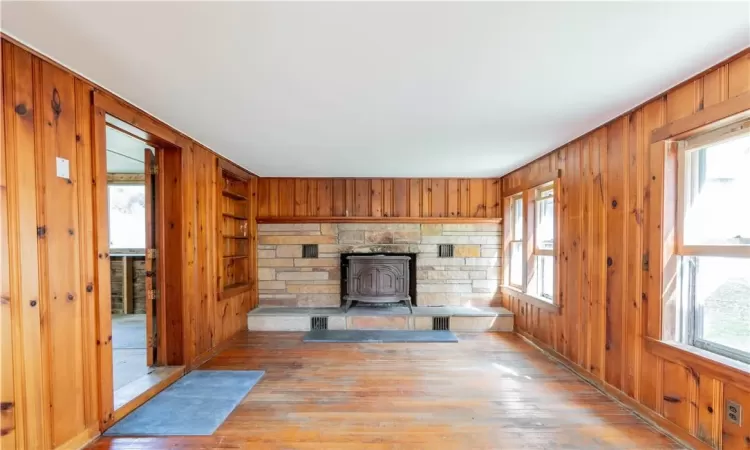 Unfurnished living room with a wood stove, light wood-type flooring, wood walls, and a healthy amount of sunlight