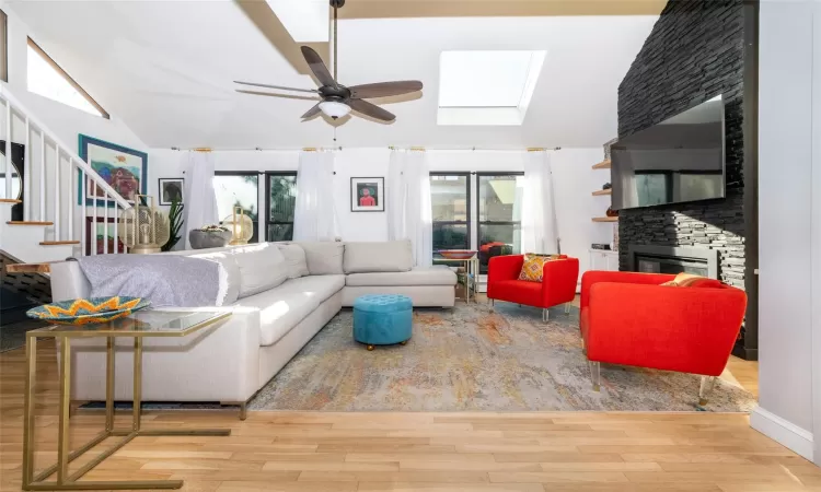 Living room featuring a fireplace, ceiling fan, light hardwood  floors, and vaulted ceiling