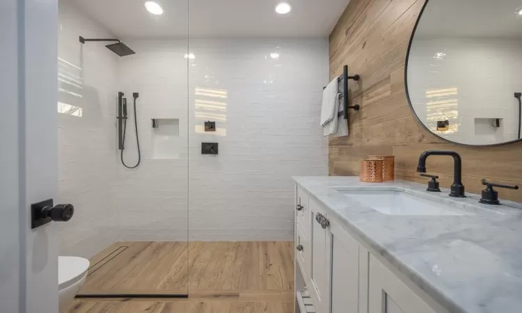 Bathroom featuring tile walls, wood-type flooring, tiled shower, vanity, and toilet