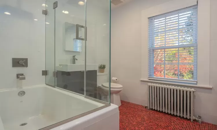 Full bathroom featuring radiator, bath / shower combo with glass door, toilet, and sink