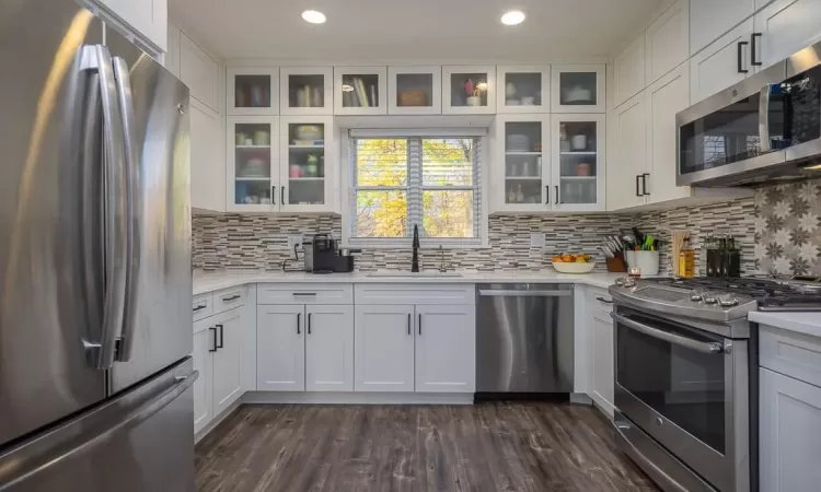 Kitchen with dark wood-type flooring, sink, backsplash, white cabinetry, and appliances with stainless steel finishes