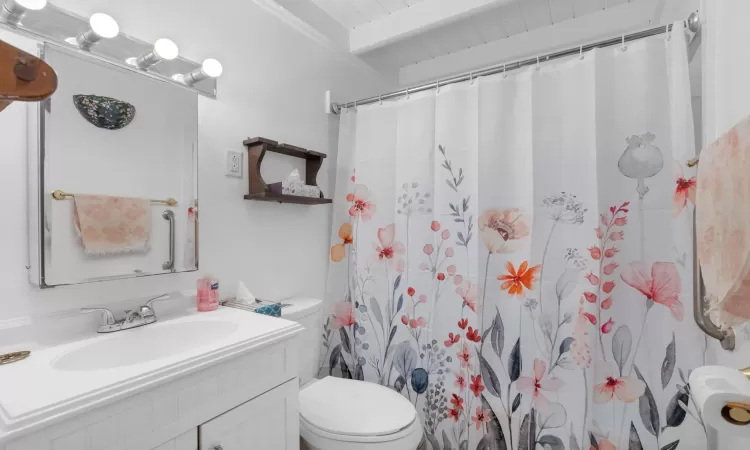 Bathroom featuring a shower with curtain, vanity, beam ceiling, and toilet