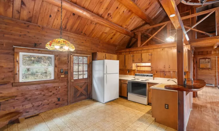 Kitchen with pendant lighting, white appliances, wood ceiling, and wood walls