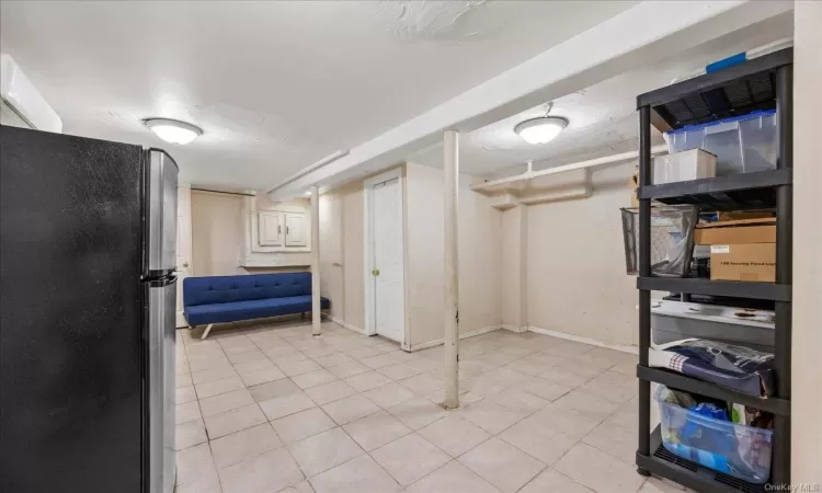 Basement with stainless steel refrigerator and light tile patterned floors