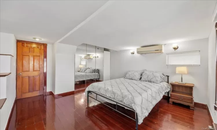 Bedroom with dark hardwood / wood-style floors and a wall unit AC