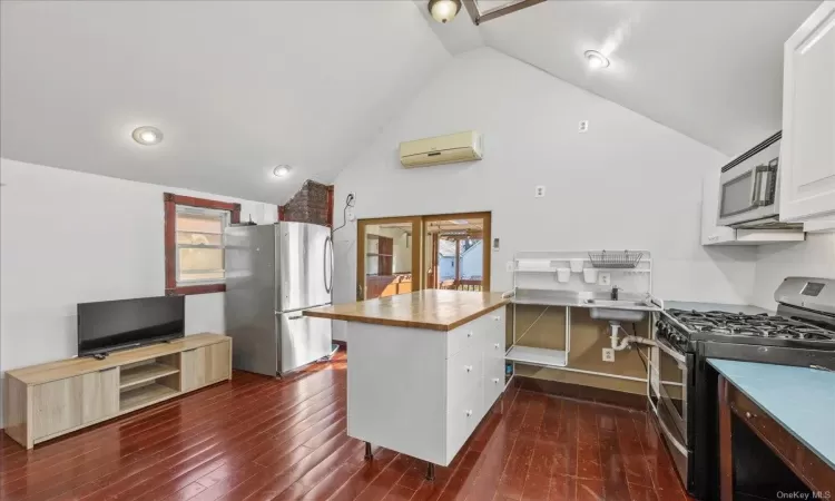 Kitchen with stainless steel appliances, dark wood-type flooring, an AC wall unit, white cabinets, and plenty of natural light