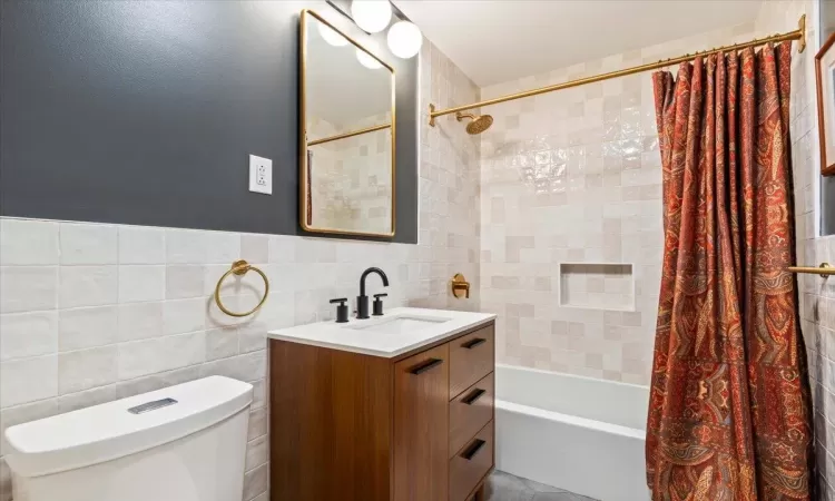 Full bathroom with vanity, toilet, shower / bathtub combination with curtain, and tile walls