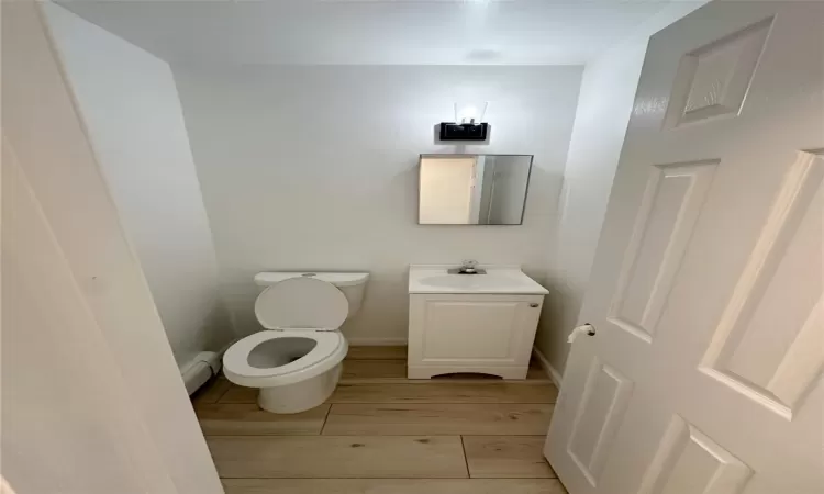 Bathroom featuring hardwood / wood-style floors, vanity, toilet, and baseboard heating