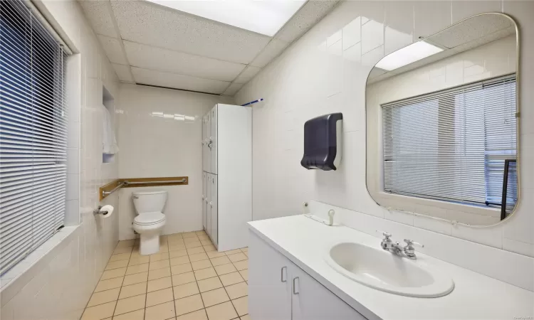 Bathroom featuring tile patterned flooring, a drop ceiling, tile walls, and toilet