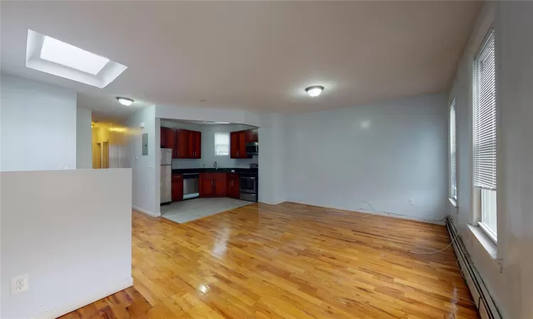 Unfurnished living room with a skylight, sink, light hardwood / wood-style floors, and a baseboard heating unit