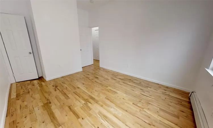 Unfurnished bedroom with a baseboard radiator and light wood-type flooring