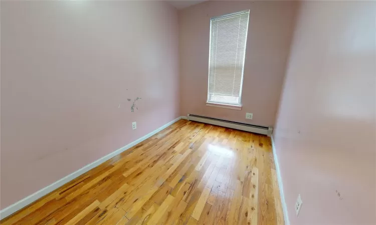 Empty room with wood-type flooring and a baseboard heating unit