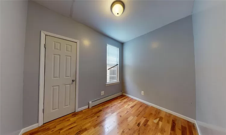 Spare room featuring wood-type flooring, baseboard heating, and vaulted ceiling