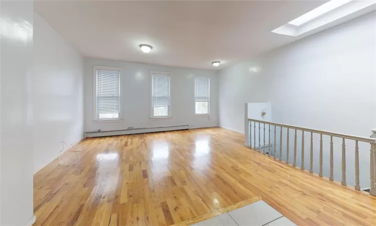 Unfurnished room featuring a skylight, baseboard heating, and light hardwood / wood-style floors