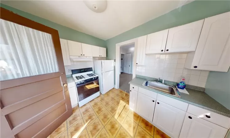 Kitchen featuring white cabinets, white appliances, sink, and backsplash