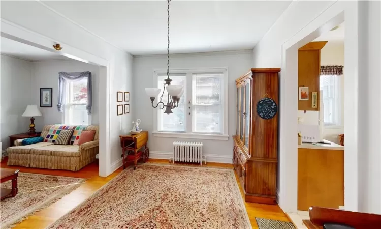 Living area featuring an inviting chandelier, radiator heating unit, light hardwood / wood-style flooring, and ornamental molding