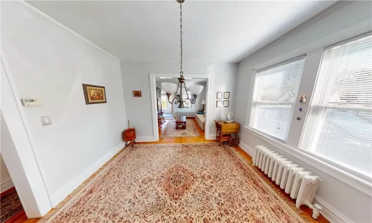 Dining room featuring light wood-type flooring, radiator heating unit, a notable chandelier, and crown molding