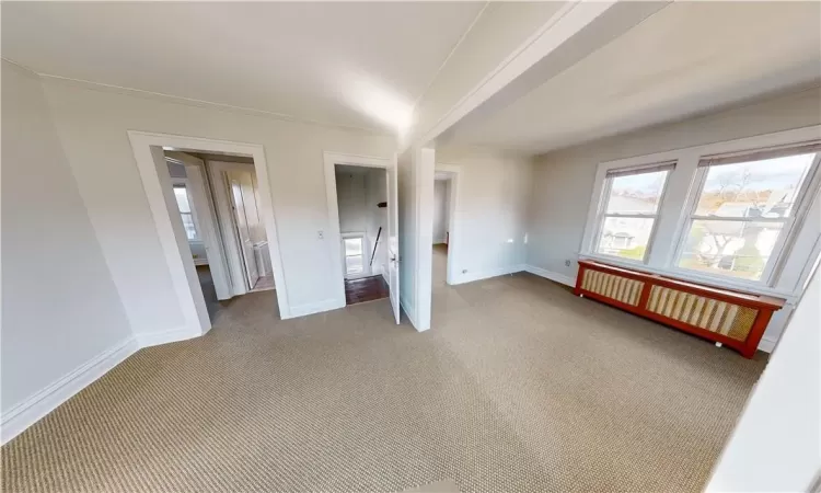 Empty room with ornamental molding, radiator heating unit, and light colored carpet