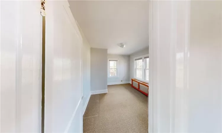 Carpeted empty room featuring radiator heating unit