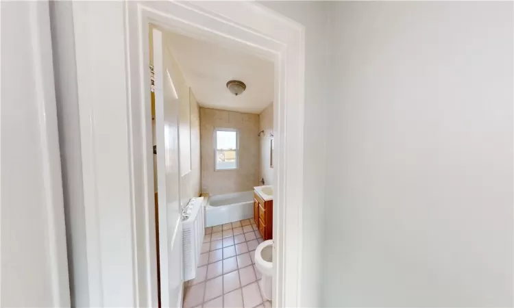 Bathroom featuring tile patterned flooring, tiled shower / bath, toilet, and radiator