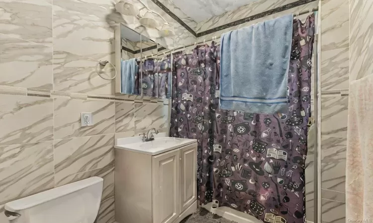 Bathroom with a shower with shower curtain, vanity, toilet, and tile walls