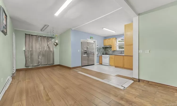 Kitchen featuring tasteful backsplash, light hardwood / wood-style flooring, a baseboard heating unit, stainless steel fridge, and white dishwasher