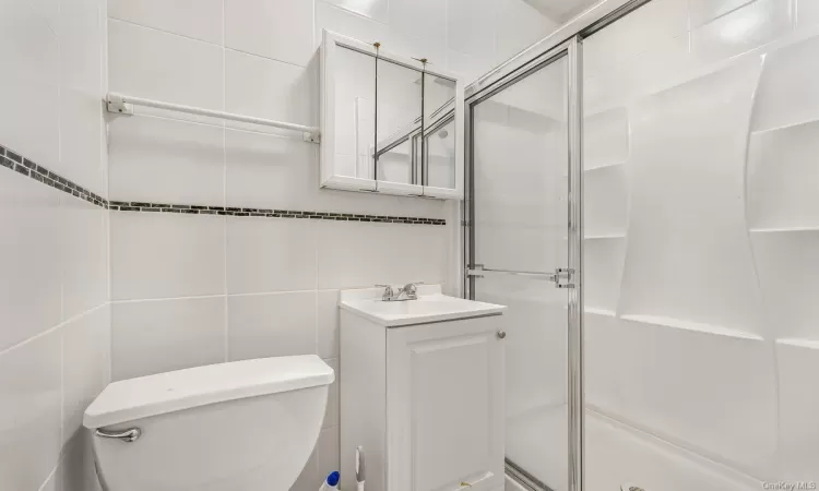 Bathroom featuring vanity, toilet, tile walls, and walk in shower