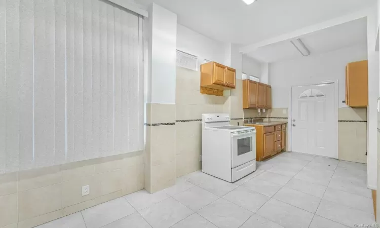 Kitchen with white range with electric cooktop, sink, light tile patterned floors, and tile walls