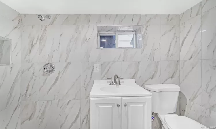 Bathroom with a shower, vanity, toilet, and tile walls