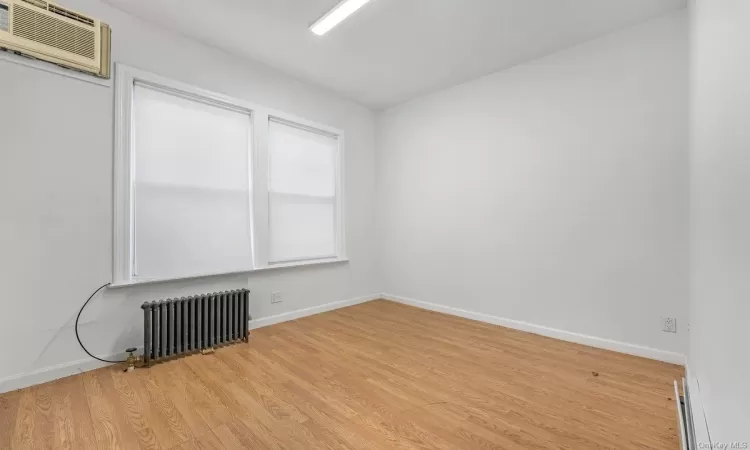 Empty room with an AC wall unit, radiator, and light hardwood / wood-style floors